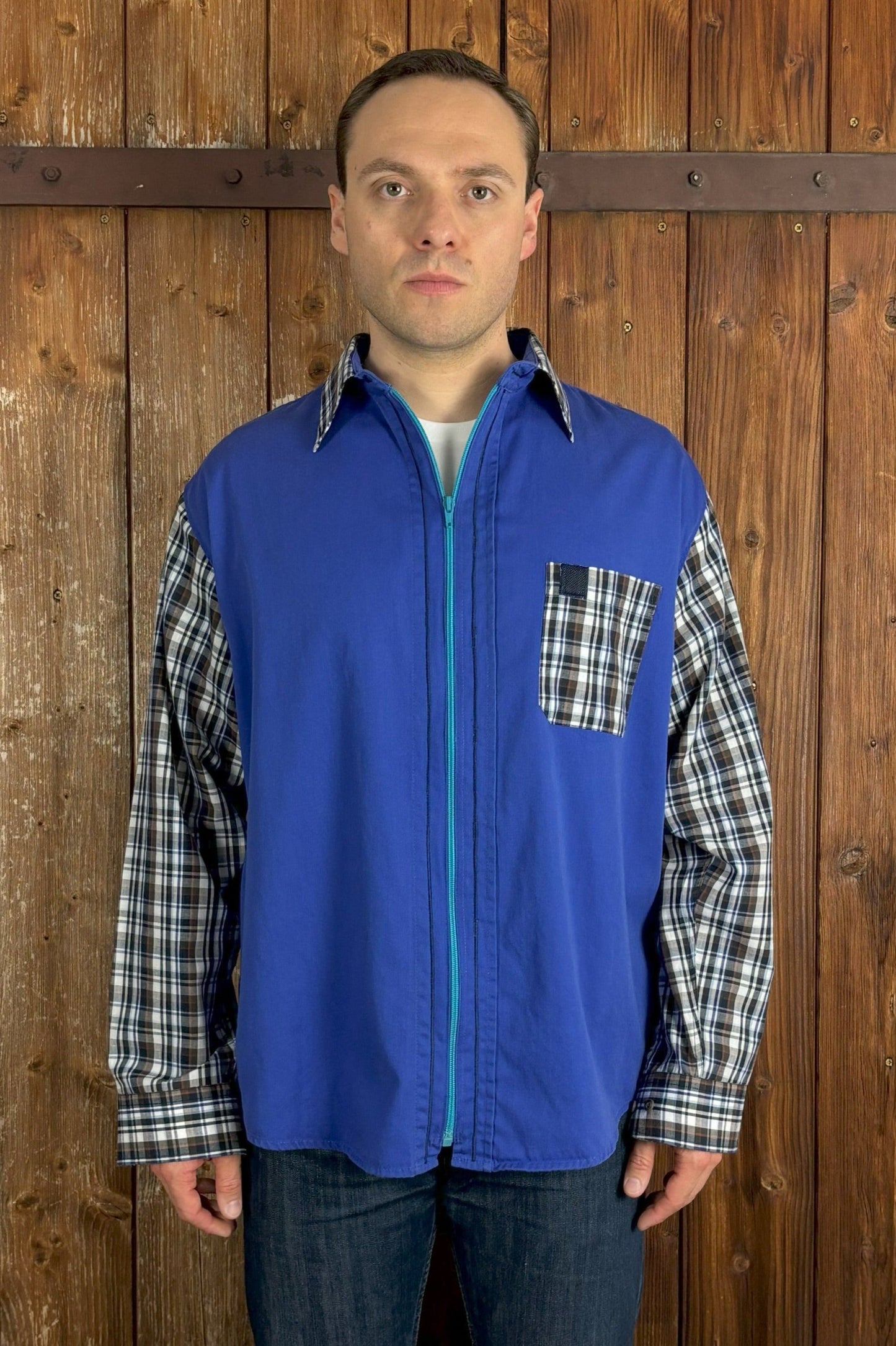 Qualitativ hochwertiges, blaues Hemd mit türkisfarbenem Reißverschluss anstelle der Knopfleiste. Kragen, Ärmel und Brusttasche wurden durch Teile eines blau-braun-weiß karierten Hemdes ersetzt. Mit Kentkragen. 