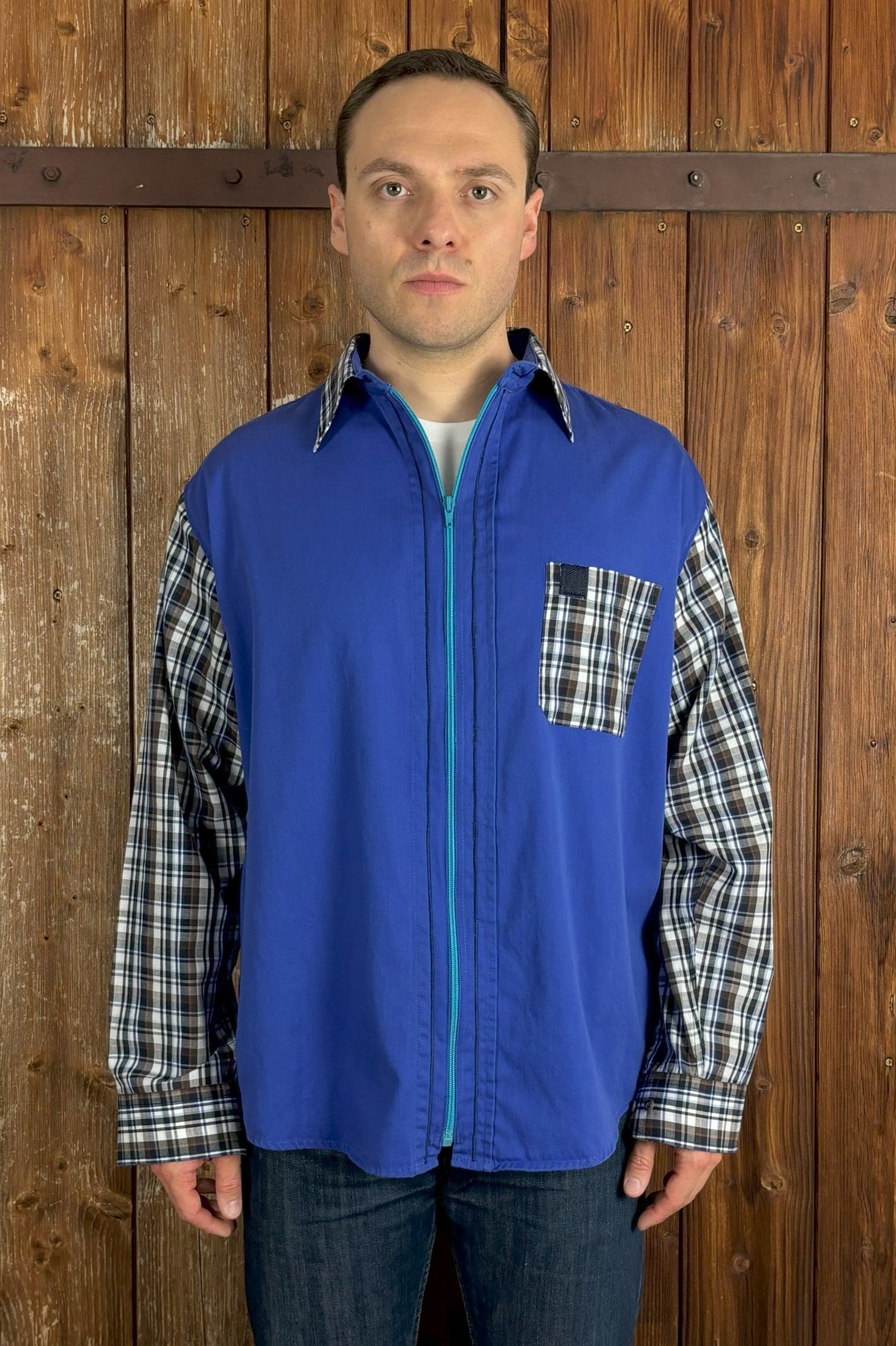 Qualitativ hochwertiges, blaues Hemd mit türkisfarbenem Reißverschluss anstelle der Knopfleiste. Kragen, Ärmel und Brusttasche wurden durch Teile eines blau-braun-weiß karierten Hemdes ersetzt. Mit Kentkragen. 